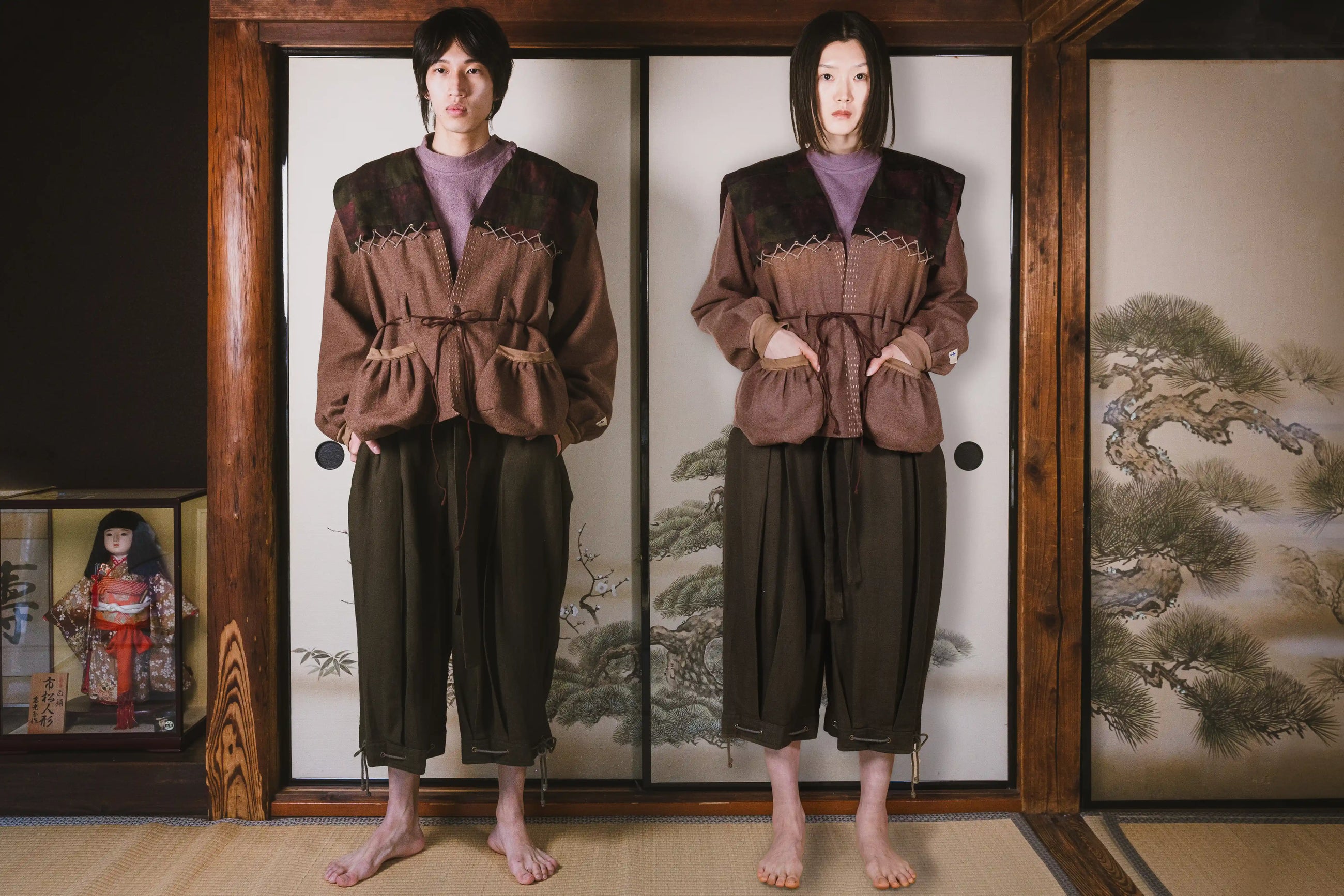 Person wearing a brown outfit standing in front of a traditional Japanese sliding door with a painting.