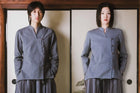 Two people wearing matching gray traditional outfits standing in front of a wooden frame.