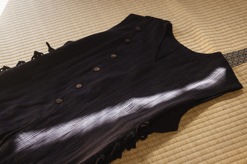 Dark sleeveless top with buttons on a textured surface