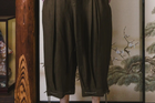 Person wearing dark green wide-leg pants standing in front of a decorative screen with floral patterns.