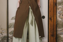 Person wearing a brown coat over a light green dress against a traditional Japanese screen background.