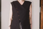 Person wearing a black sleeveless vest with buttons against a neutral background