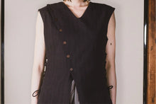 Person wearing a black sleeveless vest with buttons against a neutral background