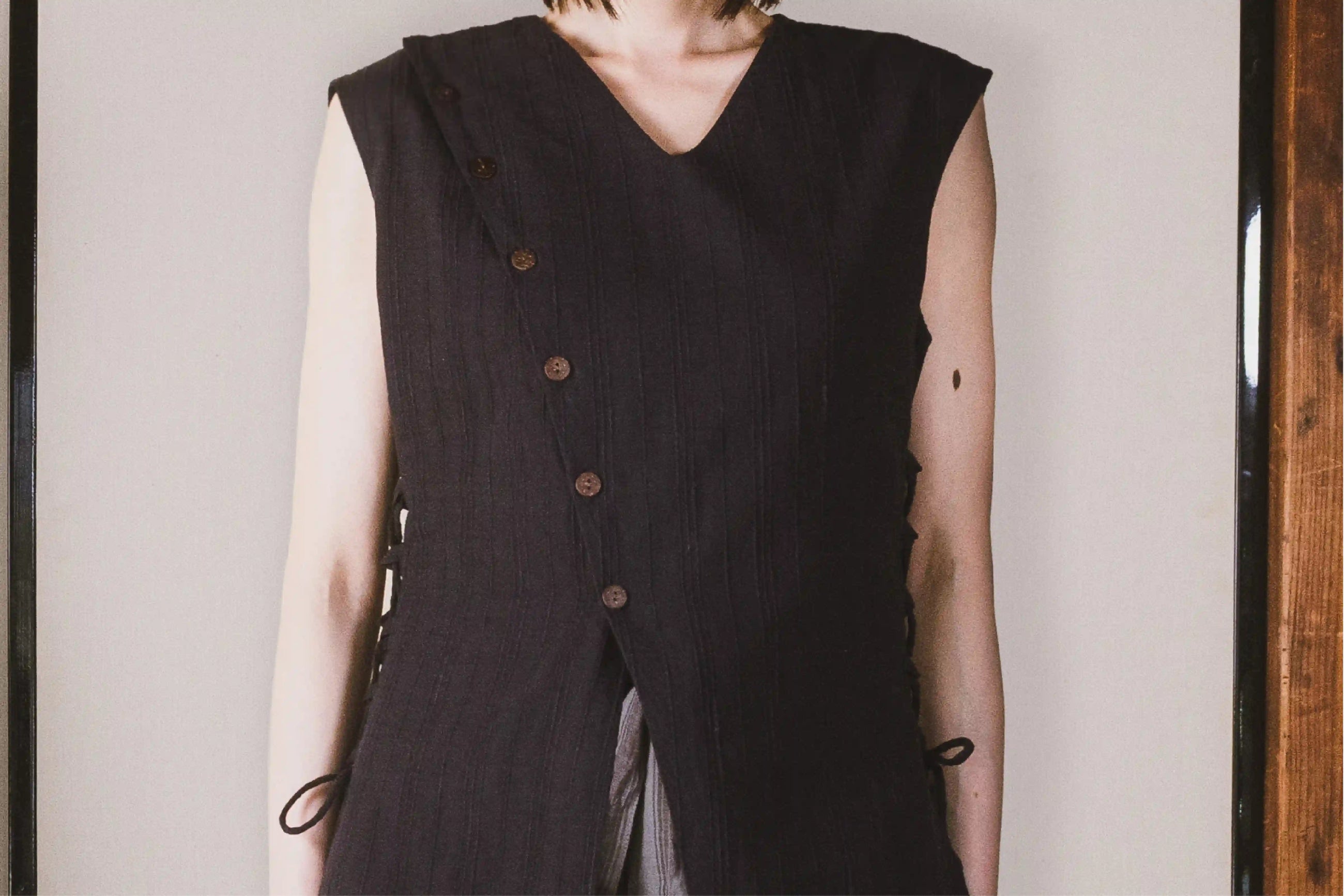 Person wearing a black sleeveless vest with buttons against a neutral background