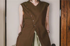 Person wearing a brown sleeveless outfit with buttons against a neutral background