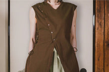 Person wearing a brown sleeveless outfit with buttons against a neutral background