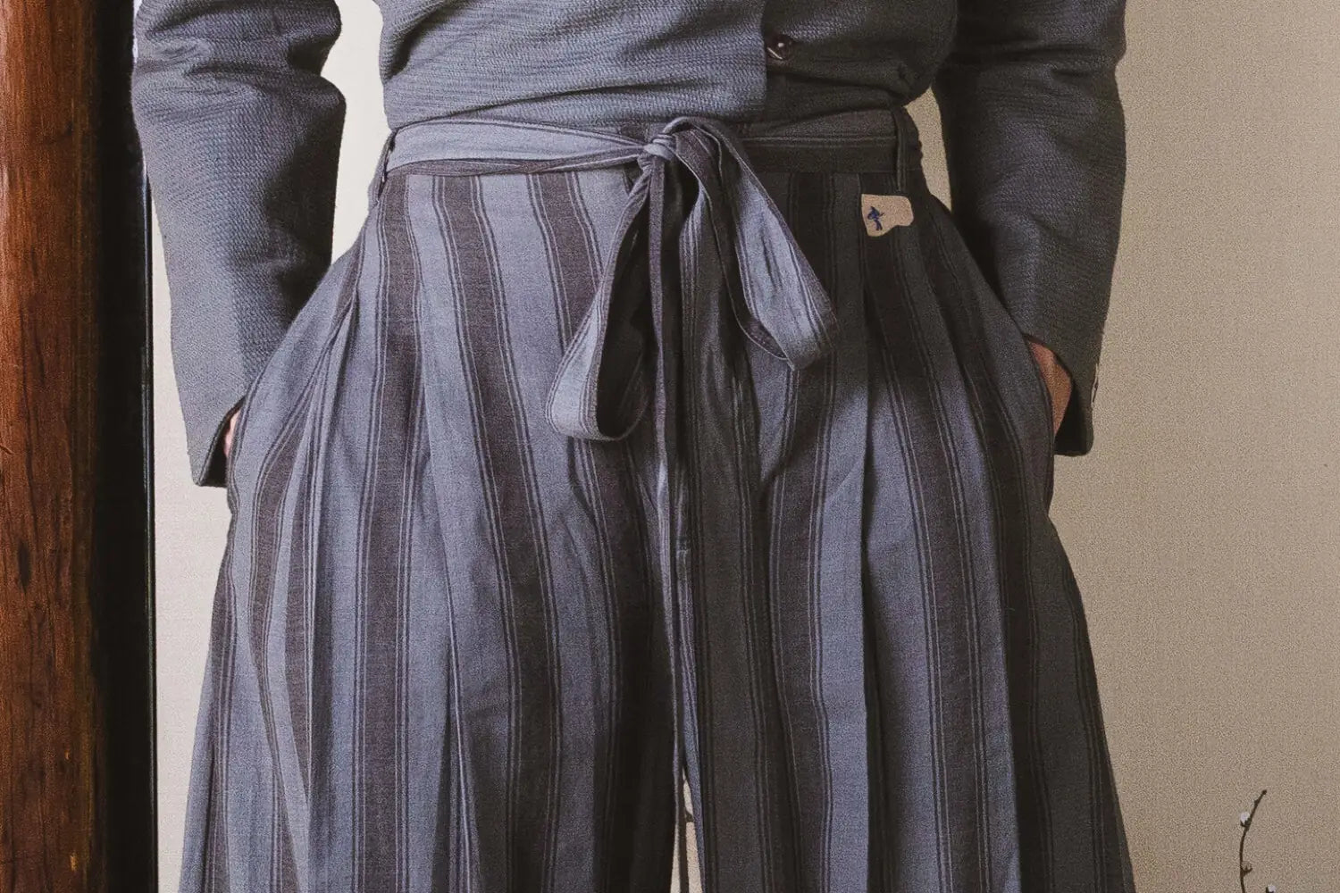 Person wearing a long coat and striped pants against a neutral background