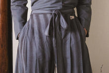Person wearing a long coat and striped pants against a neutral background