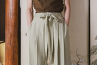 Person wearing a brown top and light green pleated pants against a neutral background