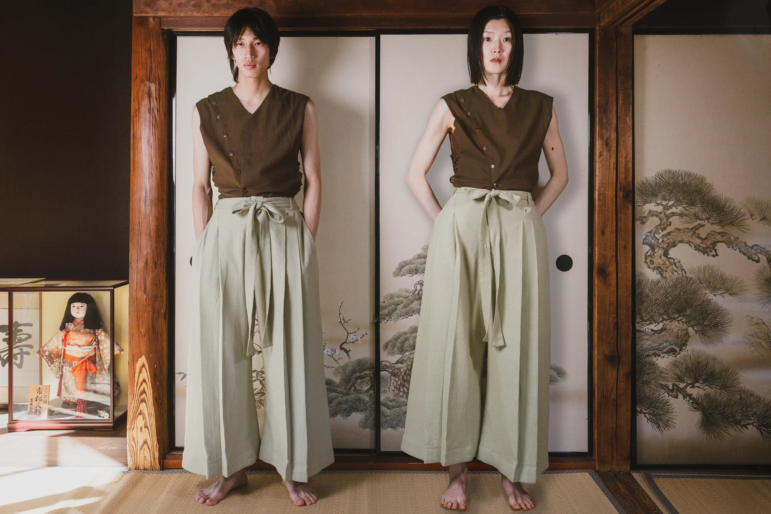 Two women in matching outfits standing in front of a traditional Japanese screen.