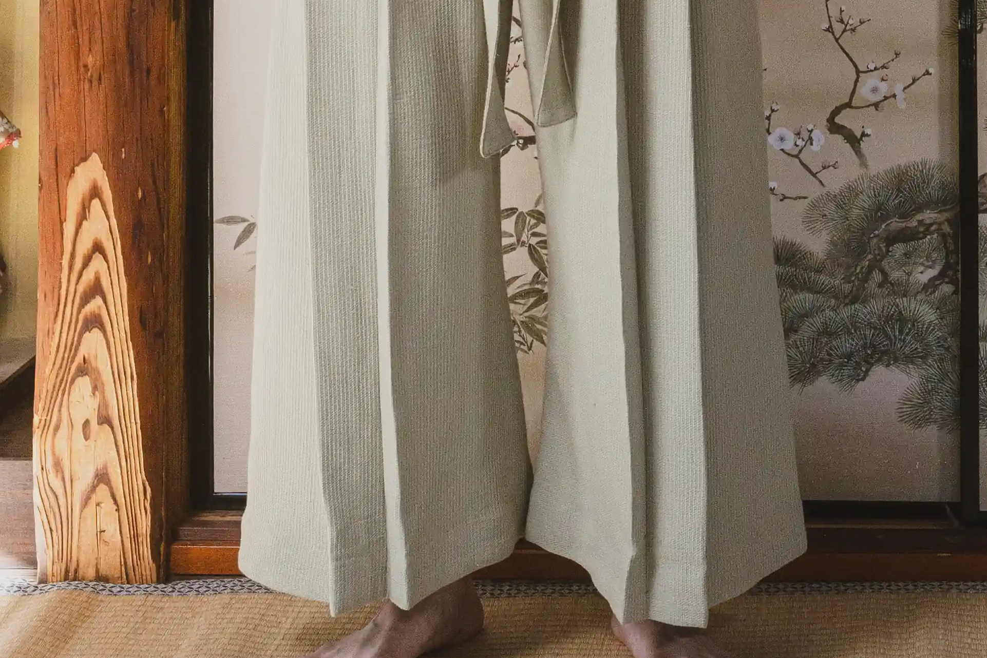 Person wearing a traditional Japanese kimono in a room with wooden floor and wall art.