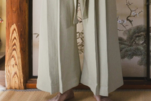 Person wearing a traditional Japanese kimono in a room with wooden floor and wall art.