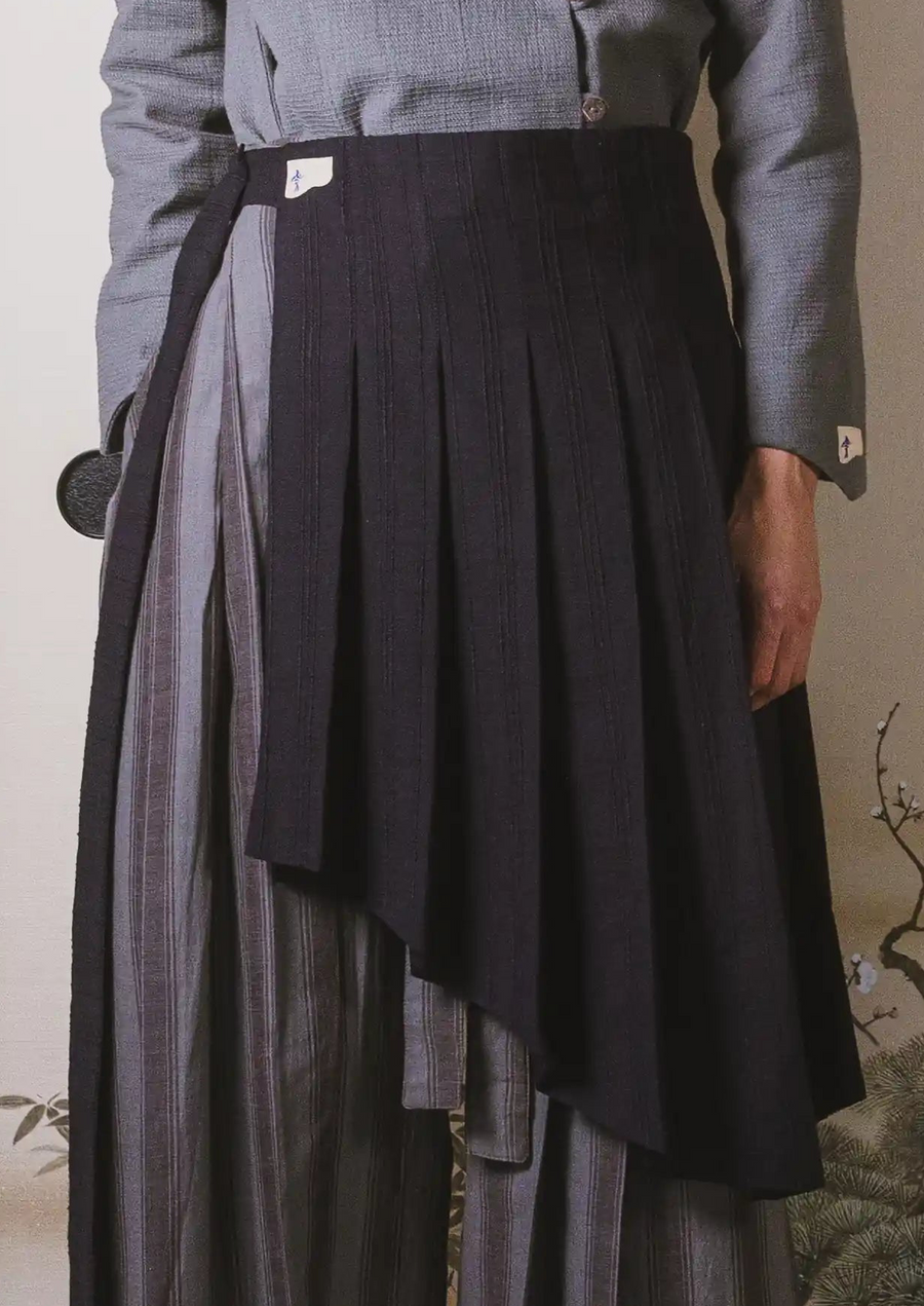 Person wearing a black pleated skirt over a gray outfit with a neutral background