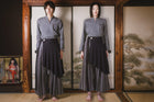 Person wearing a gray top and dark pants standing in front of a traditional Japanese screen with a wooden frame.