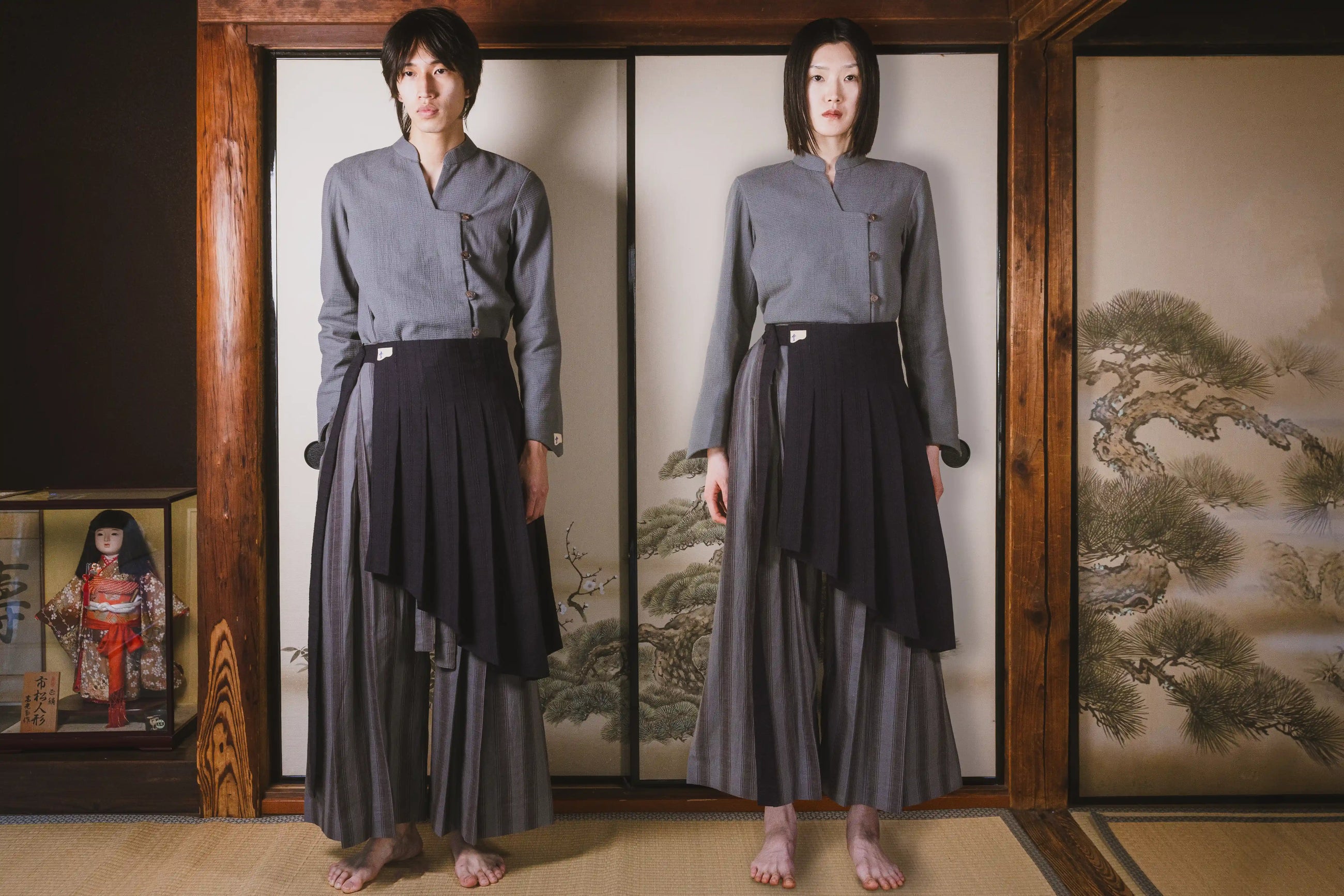 Person wearing a gray top and dark pants standing in front of a traditional Japanese screen with a wooden frame.