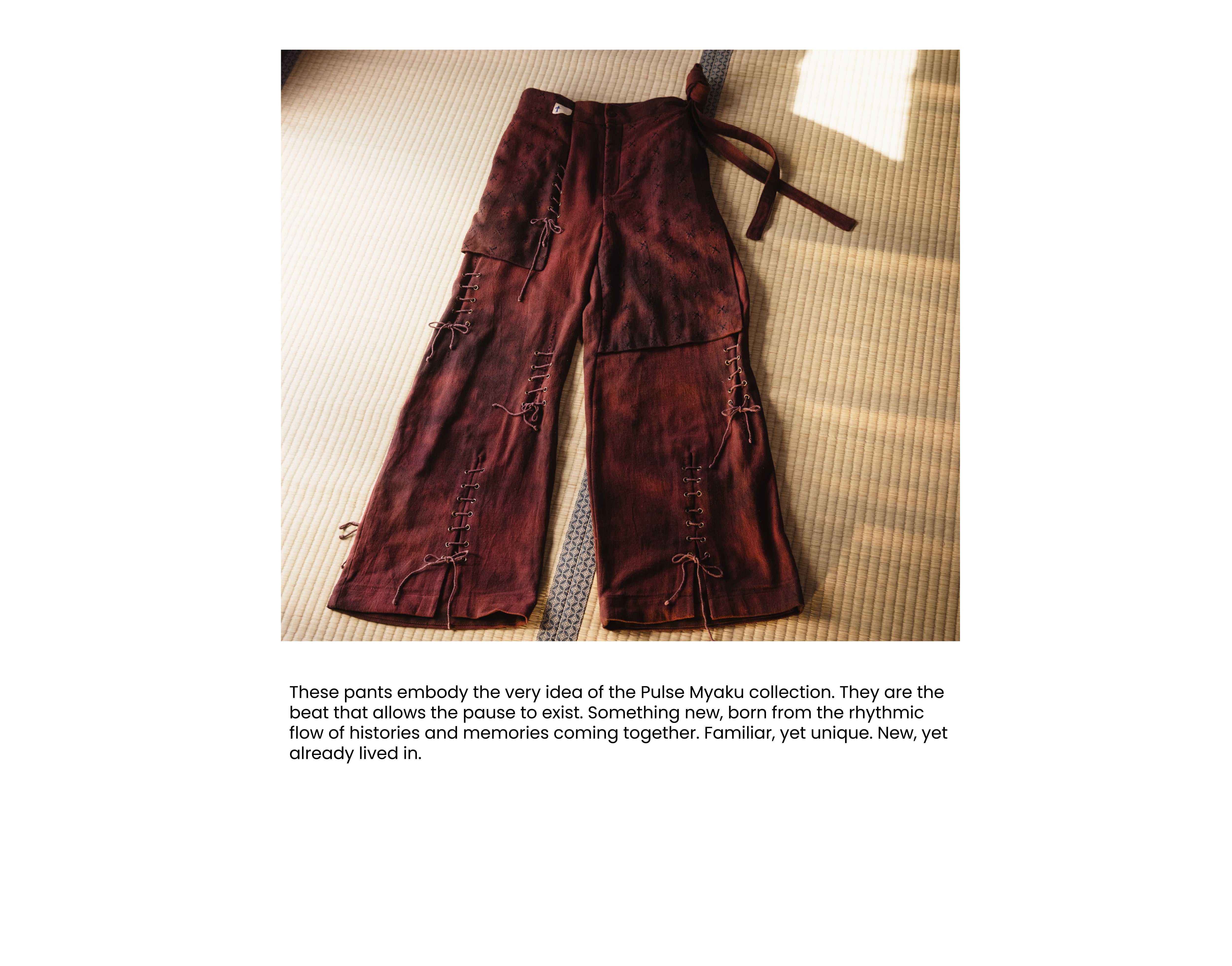 A pair of distressed, reddish-brown wide-leg trousers with unique stitched repairs and lace-up details, laid flat on a textured mat.
