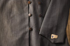 Close-up of a gray textured garment with buttons and a brand label.