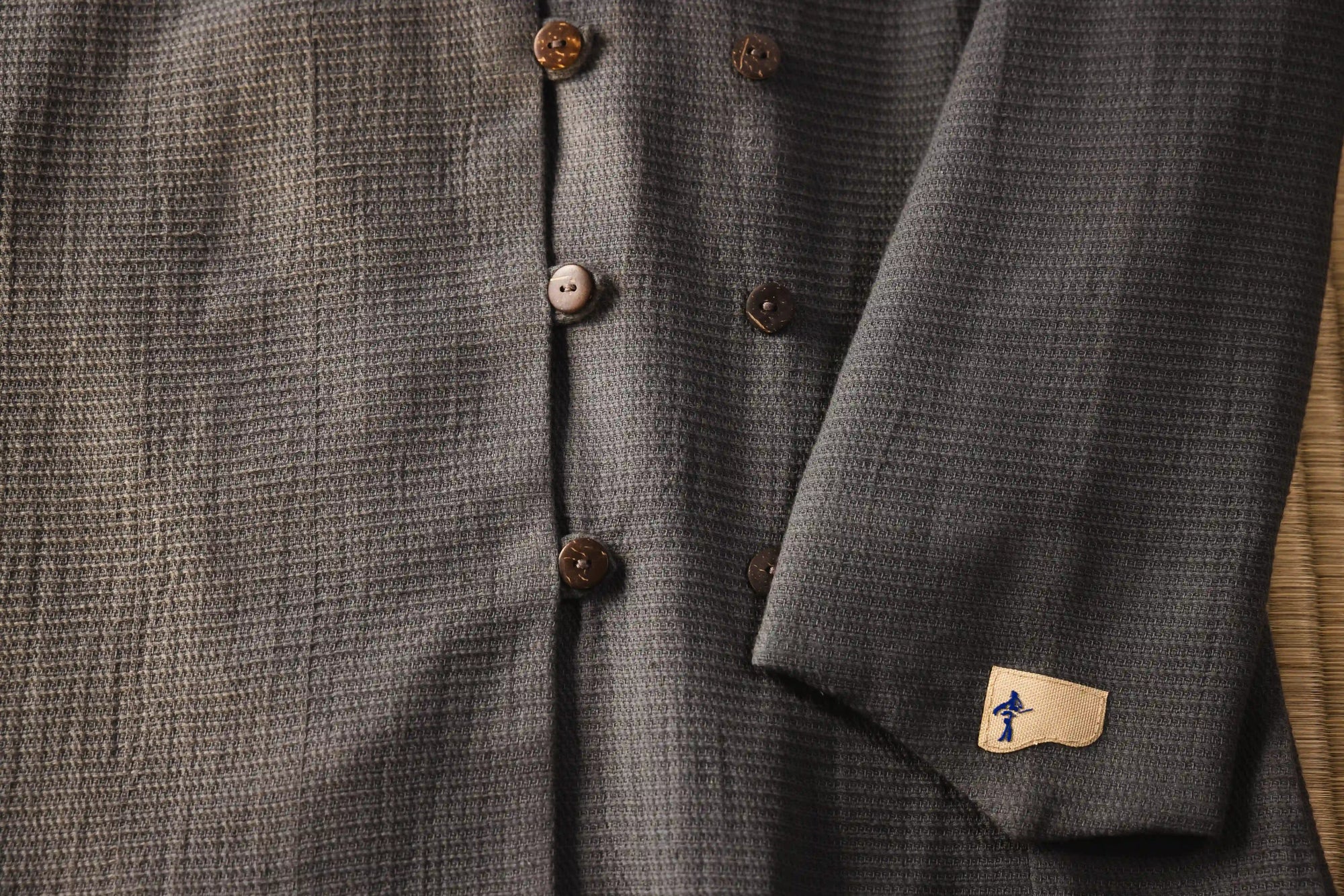 Close-up of a gray textured garment with buttons and a brand label.