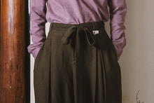 Person wearing a purple shirt and brown wide-leg pants against a neutral background