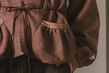 Close-up of a brown garment with a drawstring and pocket on a plain background