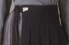 Close-up of a dark pleated skirt with a brand label on a neutral background