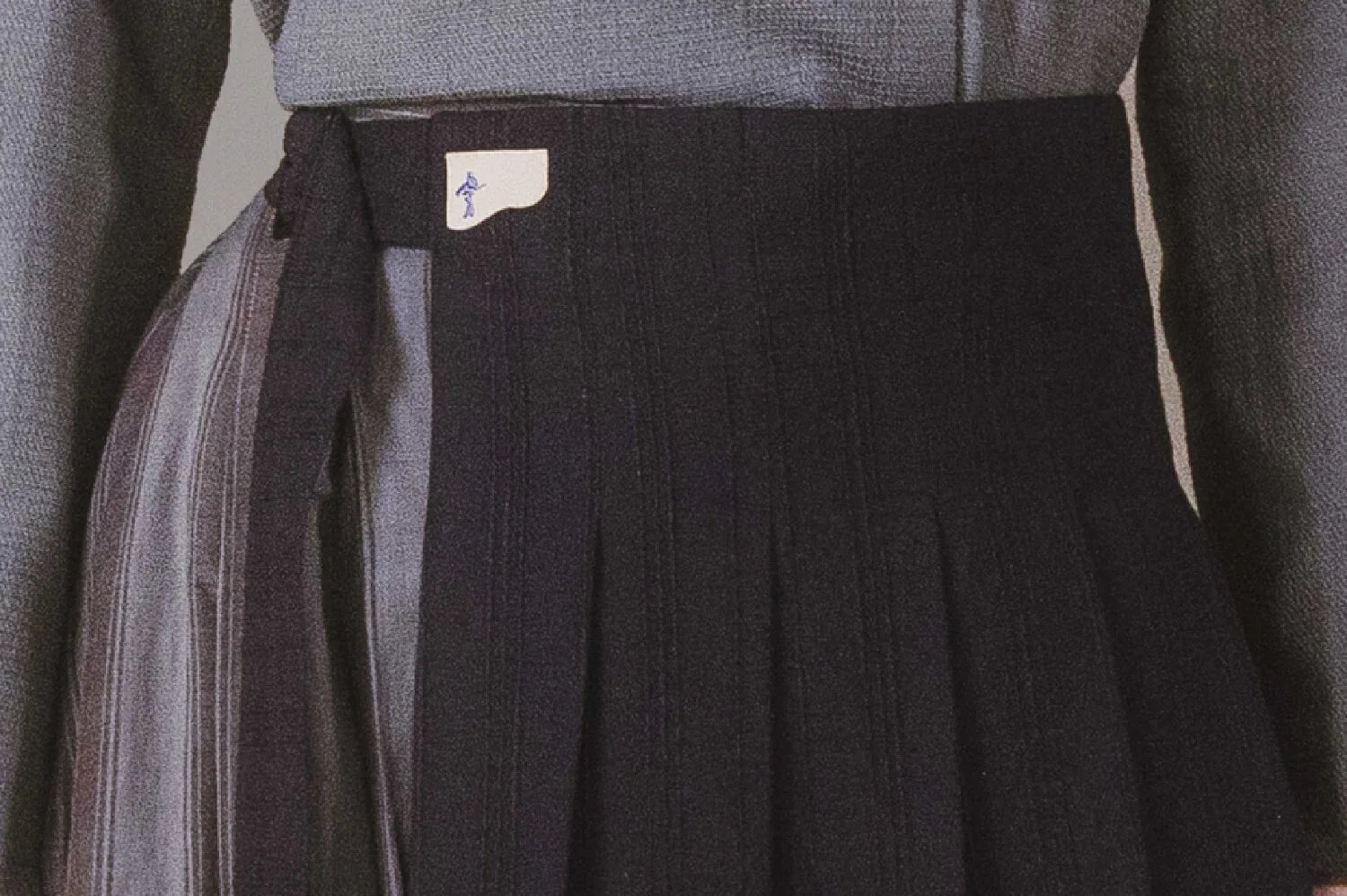Close-up of a dark pleated skirt with a brand label on a neutral background