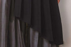 Close-up of a dark fabric draped over a striped garment against a neutral background