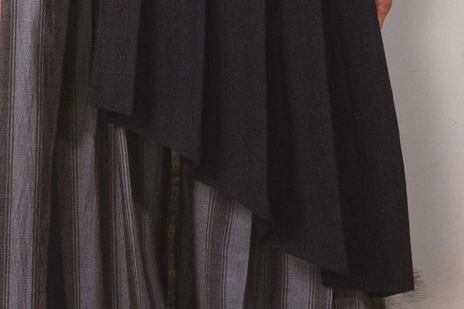Close-up of a dark fabric draped over a striped garment against a neutral background