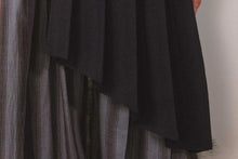Close-up of a dark fabric draped over a striped garment against a neutral background