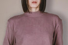 Person wearing a mauve long-sleeve top against a plain background