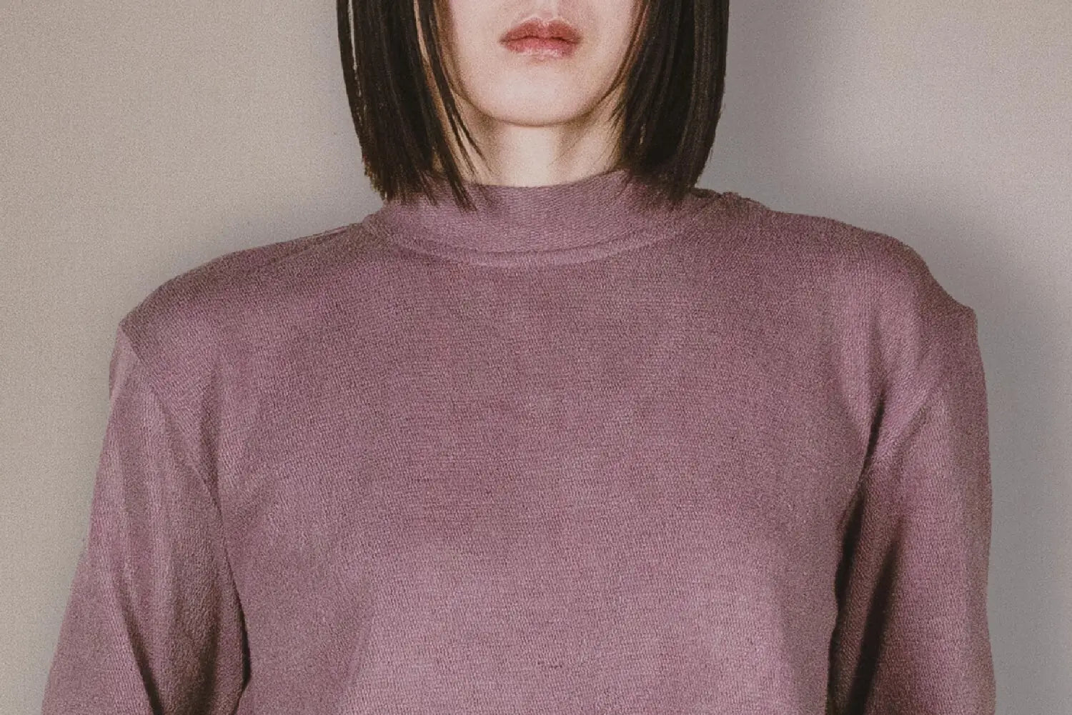 Person wearing a mauve long-sleeve top against a plain background