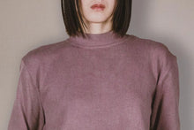Person wearing a mauve long-sleeve top against a plain background