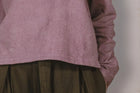 Close-up of a person wearing a mauve long-sleeve shirt and brown pleated skirt against a neutral background