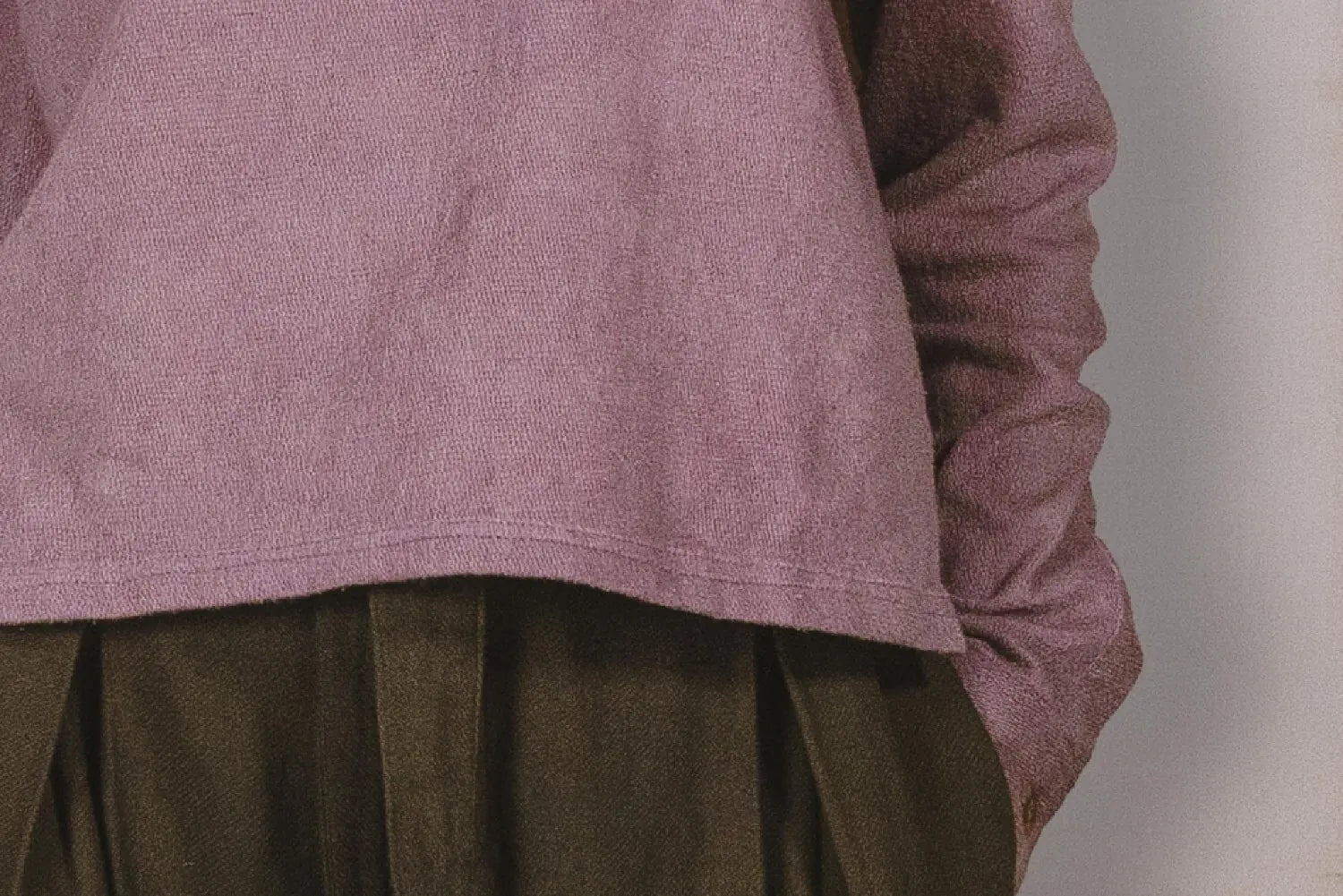 Close-up of a person wearing a mauve long-sleeve shirt and brown pleated skirt against a neutral background
