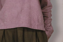 Close-up of a person wearing a mauve long-sleeve shirt and brown pleated skirt against a neutral background