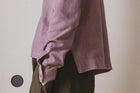 Person wearing a pink sweater over a brown garment against a neutral background